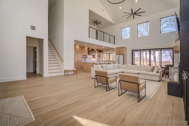 living area with light wood finished floors, visible vents, baseboards, ceiling fan, and stairway