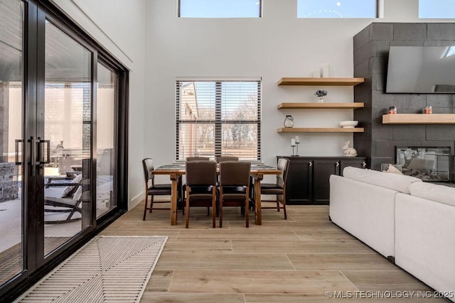 dining room with a towering ceiling, light wood-style floors, and a glass covered fireplace