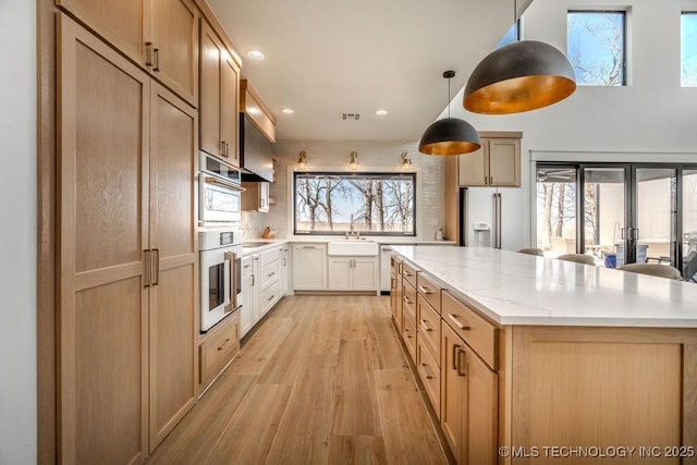 kitchen featuring a center island, high end fridge, light wood-style flooring, a sink, and light stone countertops