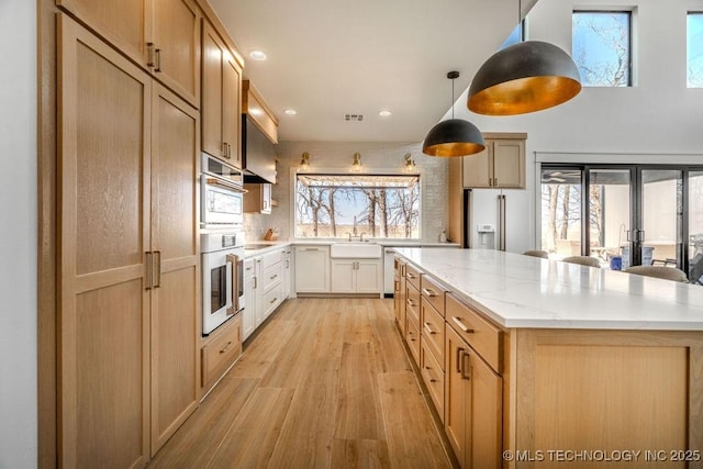 kitchen featuring high quality fridge, a sink, a kitchen island, light stone countertops, and light wood finished floors