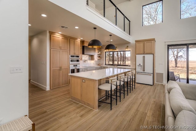 kitchen featuring visible vents, double oven, white fridge with ice dispenser, light wood-type flooring, and a kitchen bar