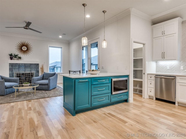 kitchen with appliances with stainless steel finishes, white cabinets, light countertops, and a tiled fireplace