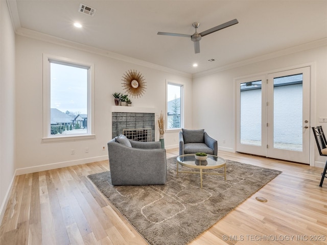 living area featuring crown molding, visible vents, light wood-type flooring, baseboards, and a tile fireplace