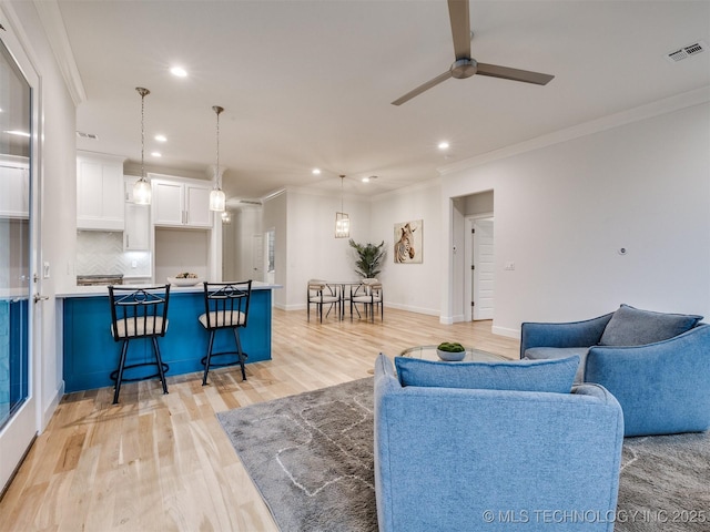 living area featuring ceiling fan, recessed lighting, visible vents, light wood-style floors, and ornamental molding