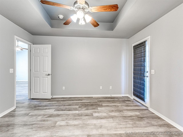 unfurnished room featuring a tray ceiling, wood finished floors, and baseboards