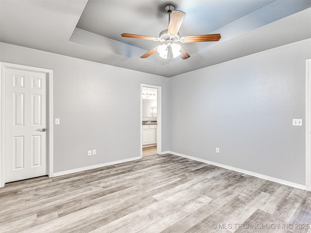 empty room featuring light wood-type flooring, baseboards, and a tray ceiling