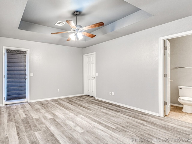 unfurnished bedroom with a raised ceiling, visible vents, light wood-style flooring, connected bathroom, and baseboards