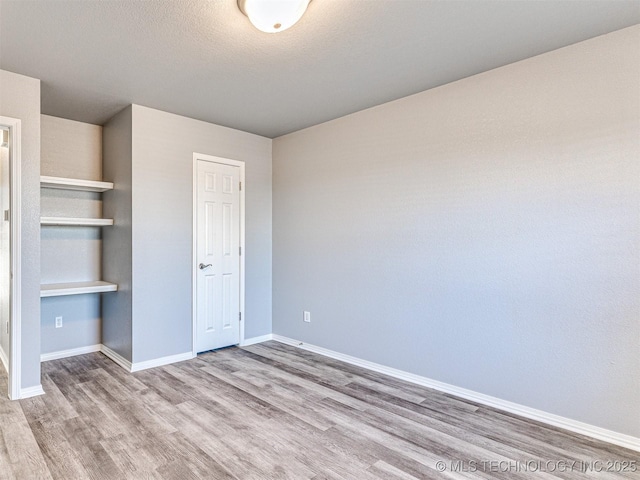 unfurnished bedroom with a textured ceiling, baseboards, and wood finished floors