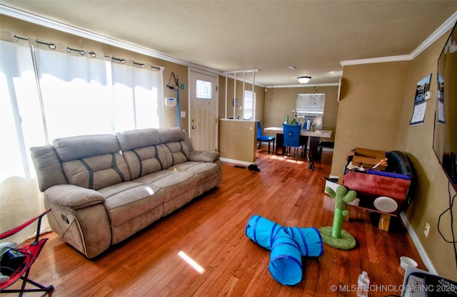 living room featuring a textured ceiling, ornamental molding, wood-type flooring, and baseboards