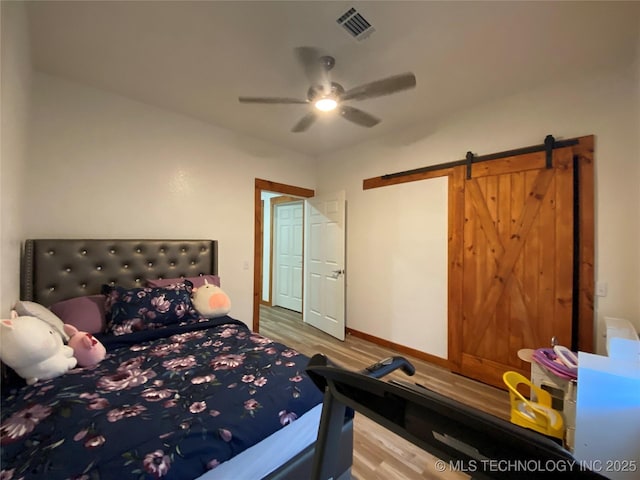 bedroom featuring a barn door, visible vents, ceiling fan, and wood finished floors