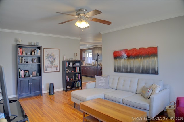 living room featuring ornamental molding, light wood-type flooring, a ceiling fan, and baseboards