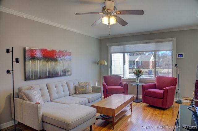 living room featuring a ceiling fan, crown molding, baseboards, and wood finished floors