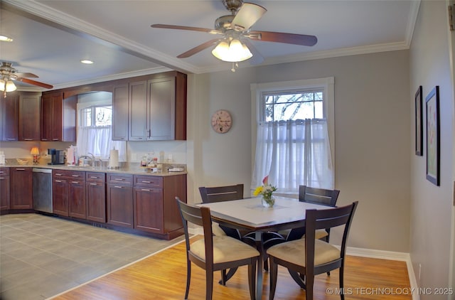 kitchen with light wood finished floors, light countertops, stainless steel dishwasher, ornamental molding, and baseboards