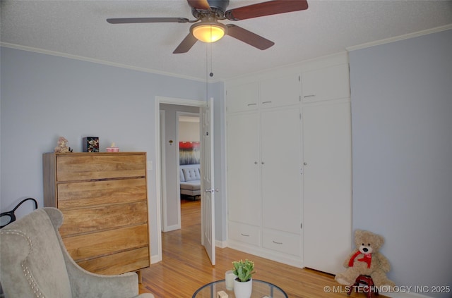 interior space with light wood-style floors, a ceiling fan, ornamental molding, and a textured ceiling