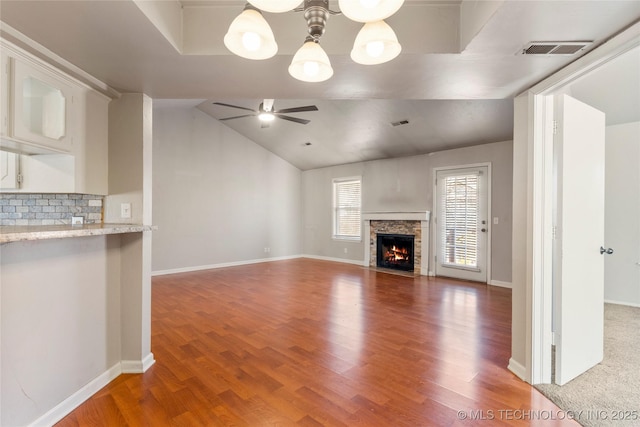 unfurnished living room with visible vents, lofted ceiling, a fireplace with flush hearth, ceiling fan, and wood finished floors