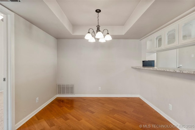 unfurnished dining area with a tray ceiling, visible vents, light wood-style flooring, a chandelier, and baseboards