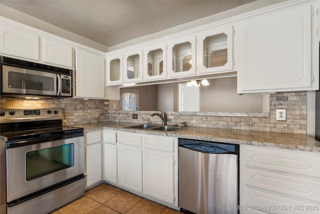 kitchen featuring light tile patterned floors, appliances with stainless steel finishes, glass insert cabinets, white cabinetry, and a sink