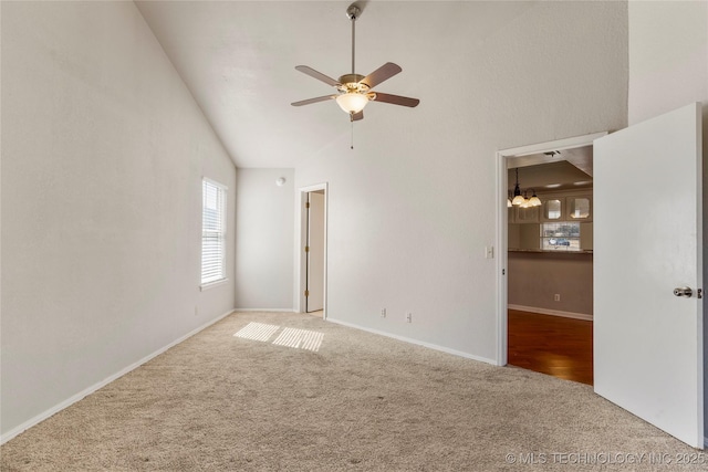 carpeted empty room featuring high vaulted ceiling, ceiling fan, and baseboards