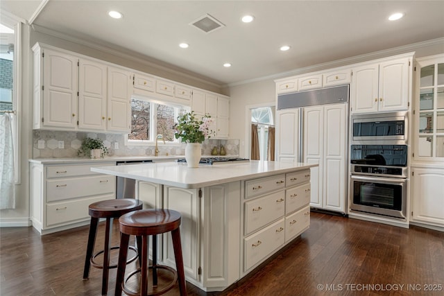 kitchen with built in appliances, a kitchen island, white cabinets, and crown molding