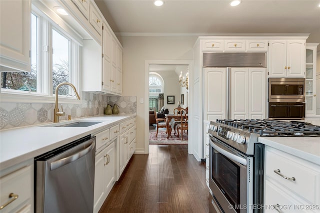 kitchen with a sink, built in appliances, white cabinetry, crown molding, and tasteful backsplash