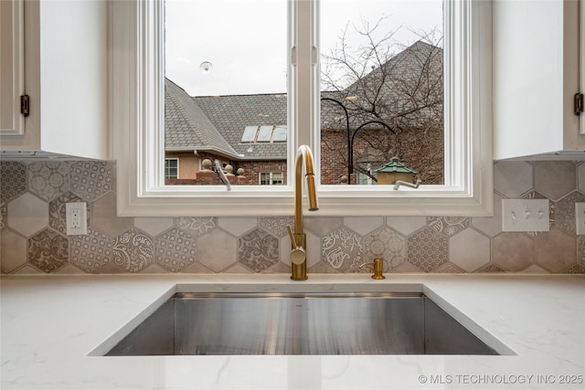 interior details with white cabinetry, light stone countertops, backsplash, and a sink