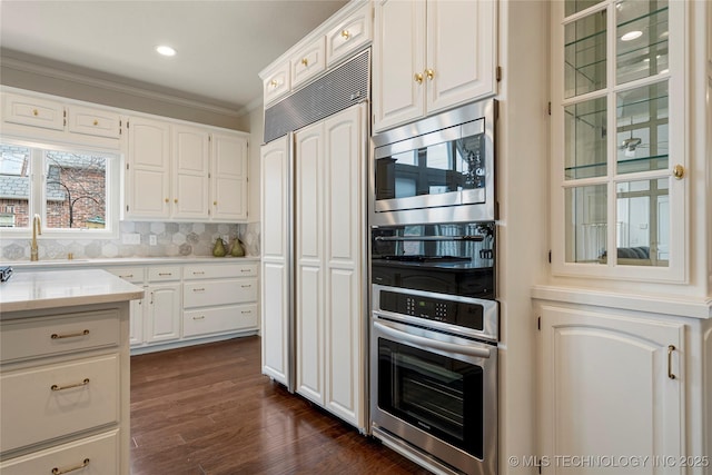 kitchen featuring backsplash, dark wood finished floors, white cabinetry, light countertops, and built in appliances