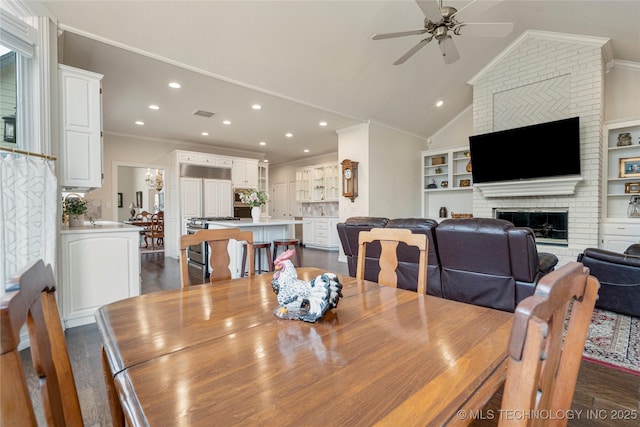 dining space featuring ornamental molding, dark wood finished floors, a fireplace, ceiling fan, and vaulted ceiling