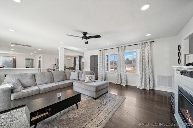 living area featuring a glass covered fireplace, visible vents, dark wood finished floors, and recessed lighting