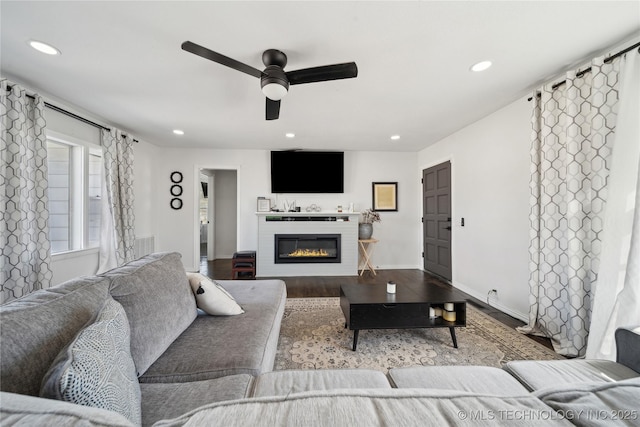 living room featuring recessed lighting, a ceiling fan, a glass covered fireplace, wood finished floors, and baseboards