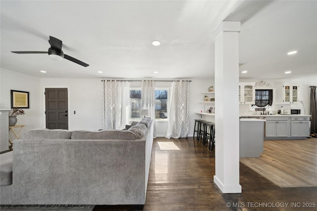 living room featuring decorative columns, baseboards, a ceiling fan, dark wood-style floors, and recessed lighting