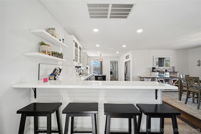 kitchen featuring open shelves, visible vents, freestanding refrigerator, white cabinets, and a sink