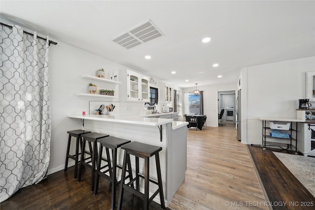 kitchen with visible vents, a kitchen breakfast bar, white cabinetry, open shelves, and glass insert cabinets