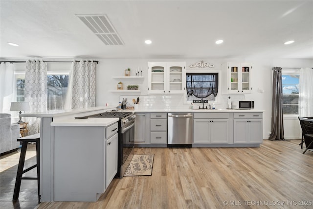 kitchen featuring open shelves, visible vents, appliances with stainless steel finishes, a peninsula, and a kitchen bar