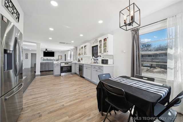 kitchen featuring light wood finished floors, recessed lighting, light countertops, appliances with stainless steel finishes, and glass insert cabinets