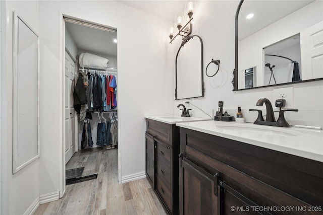 full bathroom with baseboards, wood finished floors, walk in shower, a walk in closet, and vanity