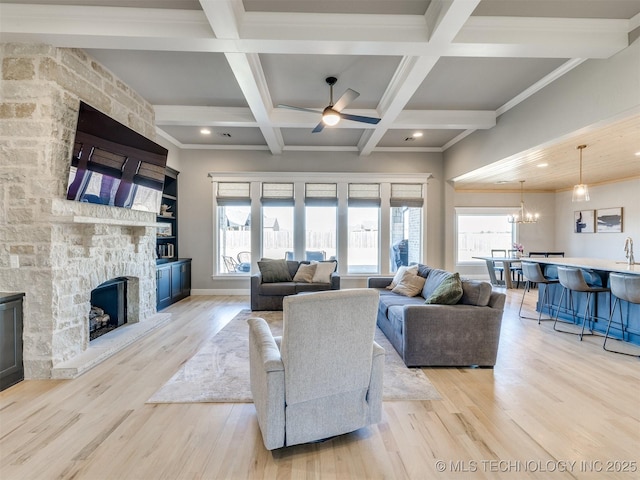 living area with light wood-style floors, a stone fireplace, coffered ceiling, beamed ceiling, and ceiling fan with notable chandelier