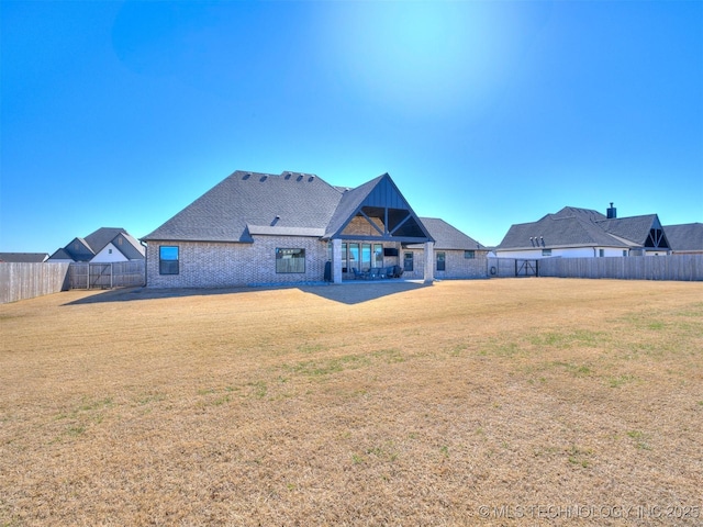 rear view of house featuring brick siding, a fenced backyard, and a yard