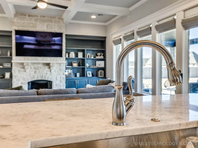 interior space with a ceiling fan, beam ceiling, coffered ceiling, and a stone fireplace