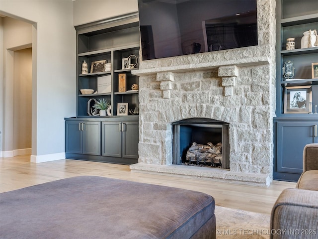 living room with a stone fireplace, built in shelves, wood finished floors, and baseboards