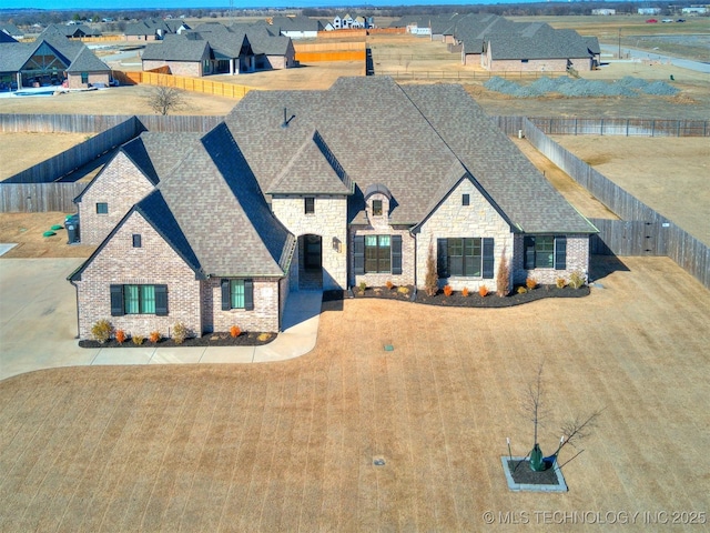 view of front of home with stone siding, roof with shingles, brick siding, and a fenced backyard