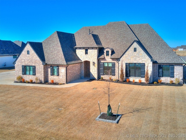 french provincial home featuring stone siding, brick siding, a front lawn, and roof with shingles