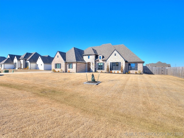 french provincial home featuring a residential view, stone siding, fence, and a front lawn