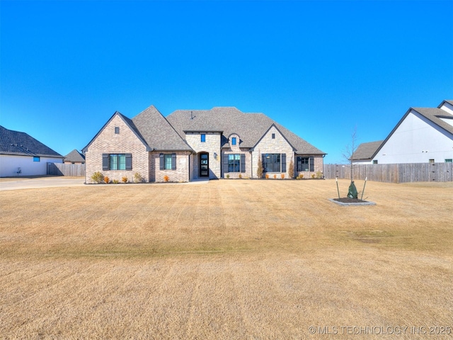 french country inspired facade with brick siding, stone siding, fence, and a front yard