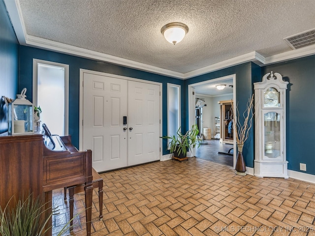 foyer featuring a textured ceiling, brick floor, visible vents, baseboards, and crown molding