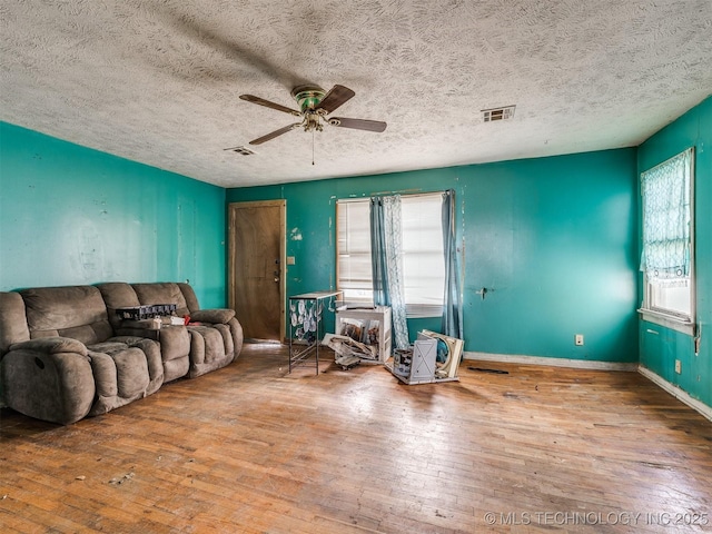 living area with a ceiling fan, visible vents, baseboards, and hardwood / wood-style flooring