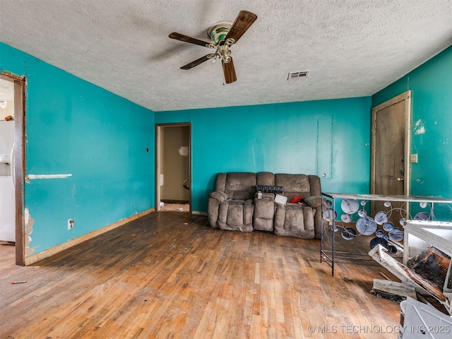 living area featuring a ceiling fan, a textured ceiling, visible vents, and wood finished floors