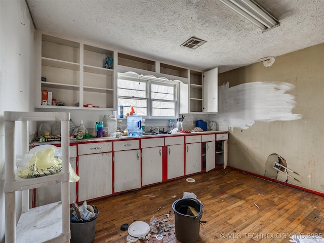 kitchen with visible vents, wood-type flooring, a textured ceiling, open shelves, and a sink