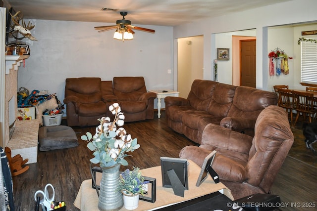 living area with visible vents, ceiling fan, a fireplace, and wood finished floors