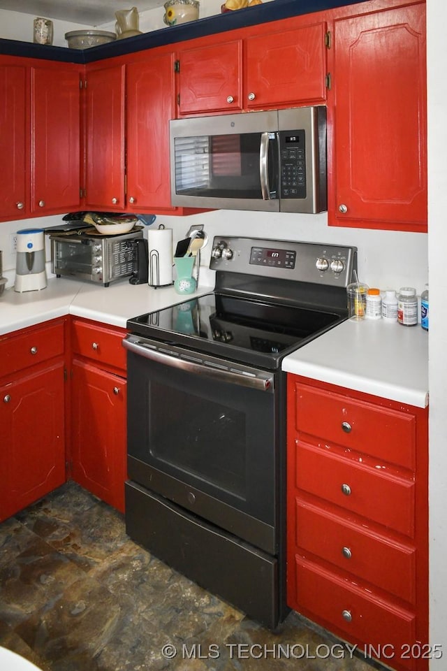 kitchen featuring a toaster, light countertops, stone finish floor, electric range oven, and stainless steel microwave