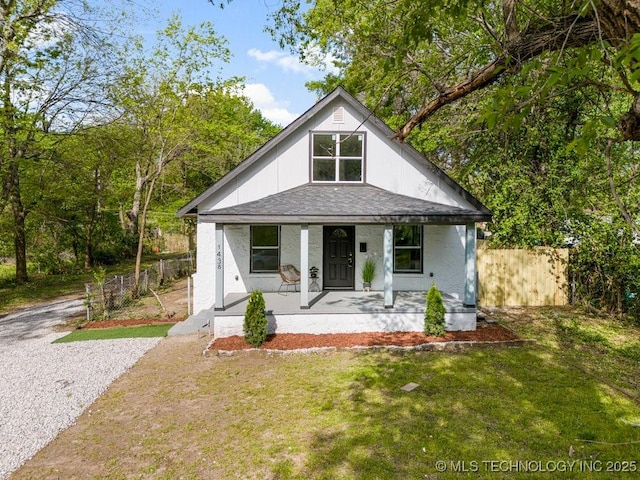 view of front of house with roof with shingles, a porch, a front lawn, and fence